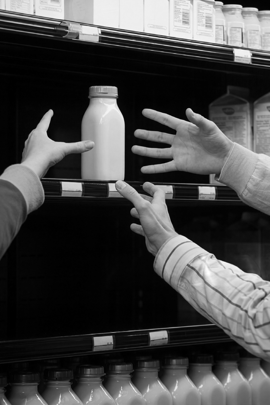 Hands reaching towards a bottle of milk on a grocery refrigerator shelf